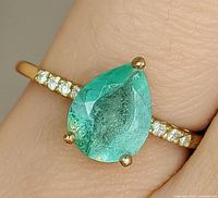 Ring on finger showing pear emerald and diamond shoulders