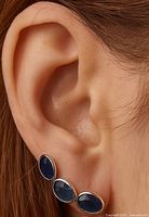 Earring worn on ear showing three oval sapphires set in white metal