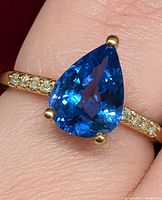 Ring on finger showing pear tanzanite and diamond shoulders