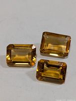 Three rectangular emerald-cut citrine gemstones on white background