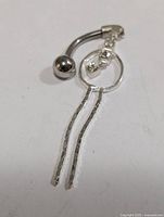 Overall view of silver belly button ring showing curved barbell, rhinestones, circular drop and two dangles