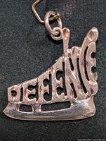 Front view of pendant showing skate shape and DEFENCE cut-out