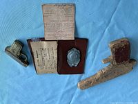 Overview showing badge in wallet with paperwork, metal pistol lighter, wooden toy gun