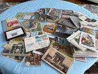 Spread of postcards, luggage labels, envelopes and framed stamp on table