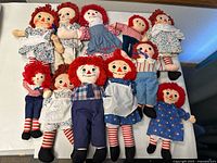 Group shot of eleven Raggedy Ann dolls on table