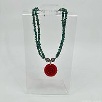 Full view of double-strand turquoise chip necklace with red flower pendant displayed on stand