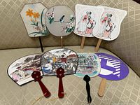 Group shot of eight handheld fans arranged on couch