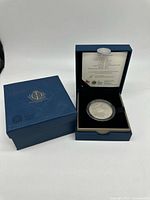 Closed outer box beside open presentation case showing coin in capsule and spec card