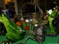 Multiple frog figurines and glass bucket grouped on table