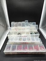 Stack of nine clear plastic locking compartment boxes filled with beads