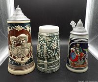 Front view of all three steins showing styles, lids and decoration