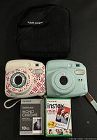 Front view of two Instax Mini 9 cameras, film packs and Case Logic bag