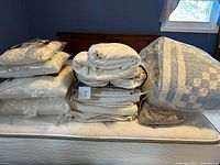 Stack of quilts and linens on mattress, blue patchwork quilt in bag visible