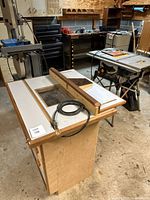 Overall view of router table in foreground, band saw and table saw visible in workshop