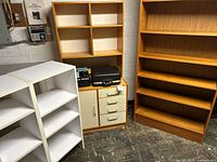 Group shot of two wood-tone and one white bookshelf, slide projector and typewriter visible on middle unit