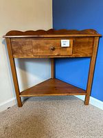 Front view of triangular wood corner accent table with drawer and lower shelf
