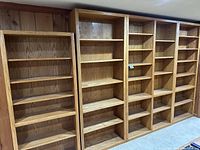 Five wood veneer bookcases side by side showing oak finish and varying widths/heights