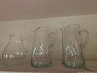 Three clear glass pitchers on shelf, shows overall lot style and sizes