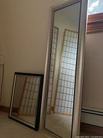 Tall silver framed mirror and smaller black framed mirror leaning against wall