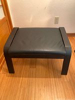 Front view of black leather ottoman on wood floor