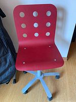 Front view of red perforated wooden swivel chair on grey base with wheels