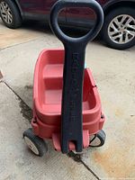 Front view showing black handle, red plastic body and wheels