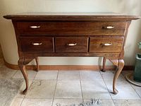 Front view of solid wood table showing four drawers, brass and ceramic pulls, Queen Anne legs