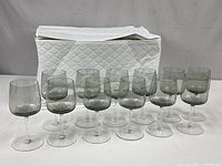 Full set of 12 smoky grey wine glasses arranged in two rows with storage case behind