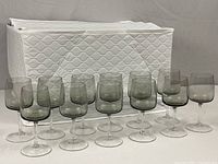 Group of 12 smoky crystal wine glasses arranged in front of white quilted storage case