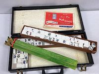 Open carrying case showing white Mah Jongg tiles, green rack, and instruction booklet