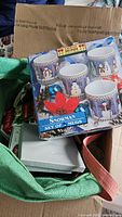 Box showing set of two snowman mugs inside tote with other items