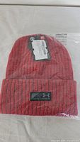 Front view of beanie in sealed bag showing color, rib knit, cuff and logo patch