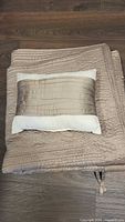 Folded quilted taupe bedspread with accent pillow on top