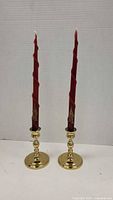 Pair of brass candlesticks each holding a red spiral taper candle