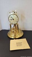 Front view of brass anniversary clock under glass dome with instruction booklet