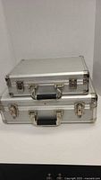 Two stacked silver aluminum briefcases showing size difference, exterior condition, latches and handles