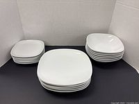 Three stacks of white square dinnerware showing dinner plates, side plates and bowls