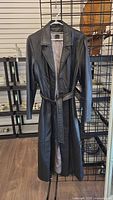 Full view of black leather coat hanging showing length and belt