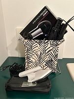 Boxed InfinityPRO by Conair hair dryer, patterned bin holding two umbrellas, travel iron with pouch in foreground