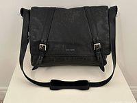 Front view showing flap, buckle straps, shoulder strap, Cole Haan logo