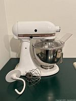 Side view of mixer with bowl, splash guard, dough hook, wire whisk