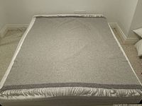 Full view of grey and white throw blanket laid flat showing size and fringe