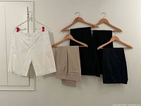 Group shot showing white shorts and three pairs of dress pants in beige, black and navy on hangers