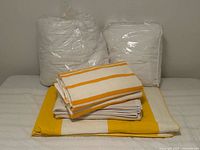 All items grouped: two packaged white duvet covers, folded striped towels, cream blanket, yellow & cream coverlet