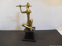 Front-left view of brass flute player on black tiered base