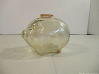 Left side view of clear glass pig bank showing textured surface and amber slot