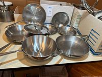 Assorted stainless skillets and lids on table