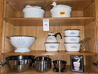 Cabinet view showing Apilco casseroles with animal lids, enameled colander, Corning Ware pieces partially visible