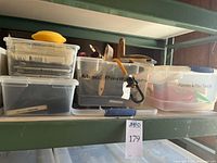 Clear bins on shelf containing bristle brushes, funnels, pour spouts, misc tools