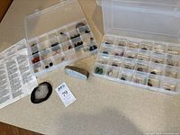 Two open clear plastic cases showing numerous mineral specimens, loose geode slice and paper list on tabletop